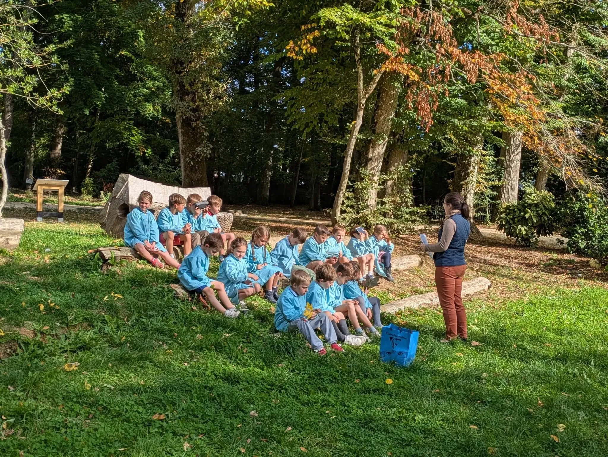 Une classe travaille dehors avec sa maîtresse, dans le parc