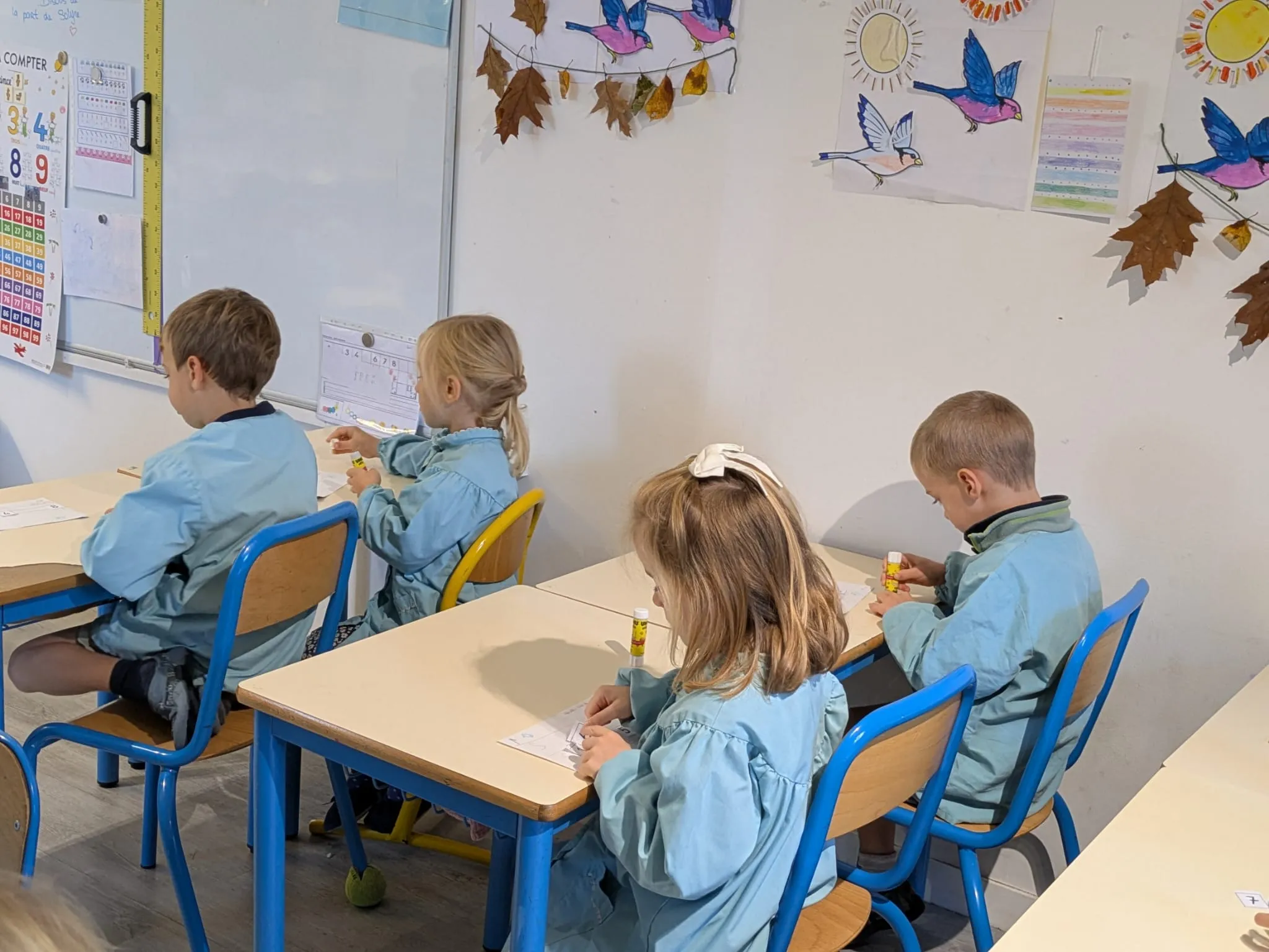 Élèves de maternelle au travail, sous les oiseaux peints de la classe