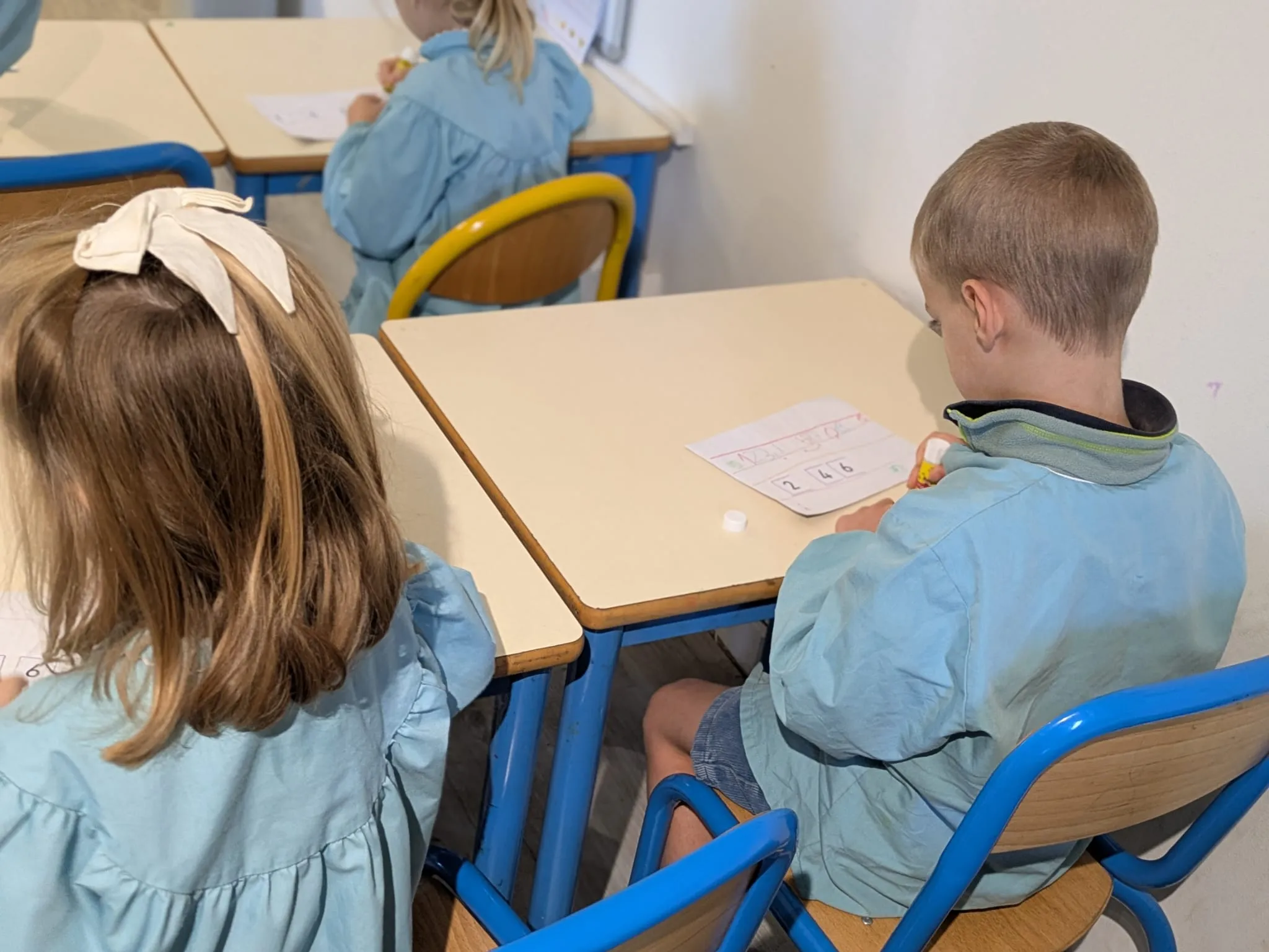 Élèves de maternelle penchés sur leur fiche de nombres