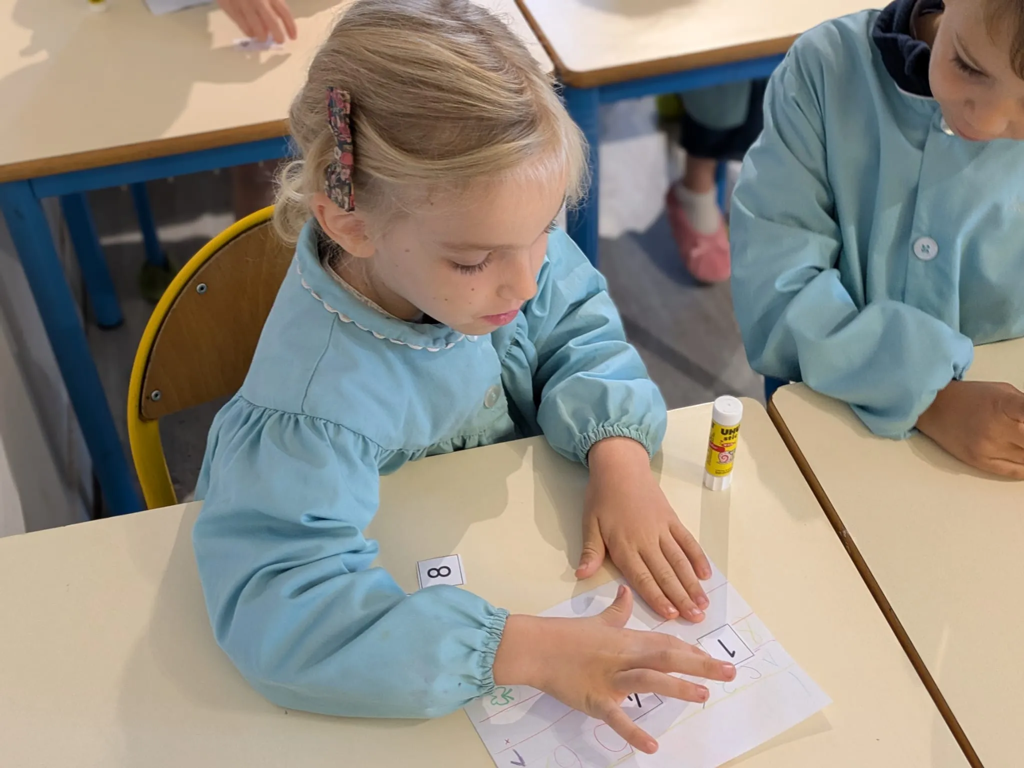 Une élève de maternelle colle les nombres sur sa fiche